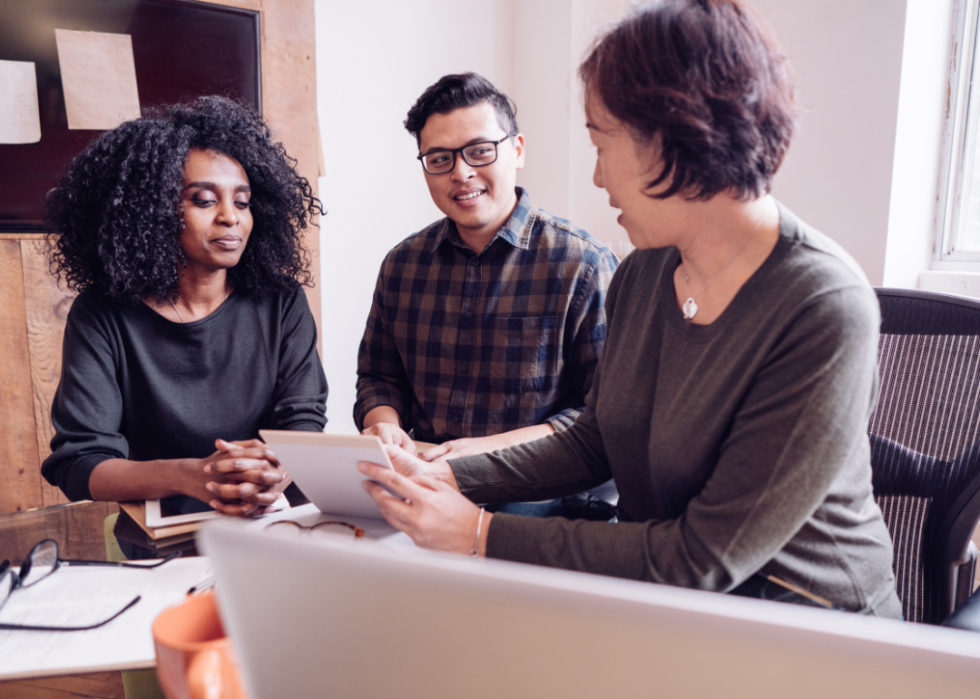 An accountant sitting at a desk with her face towards a couple sitting in her office explaining taxes.