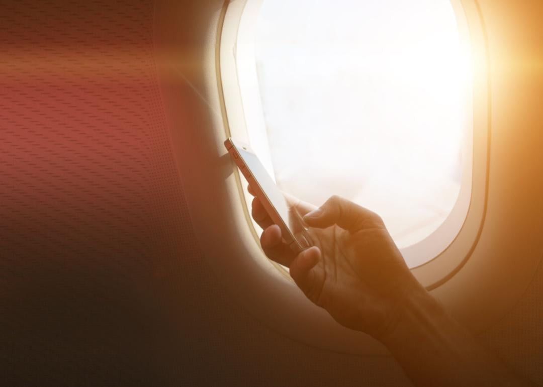 A person holding a phone next to an airplane window.
