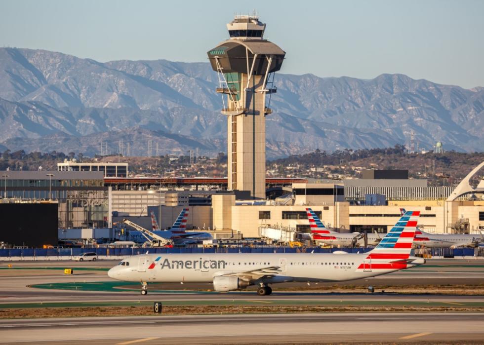 American Airlines airplane parked at a gate. There is a tall control tower in the background with a dome structure on top. Behind the tower there are mountains in the distance.