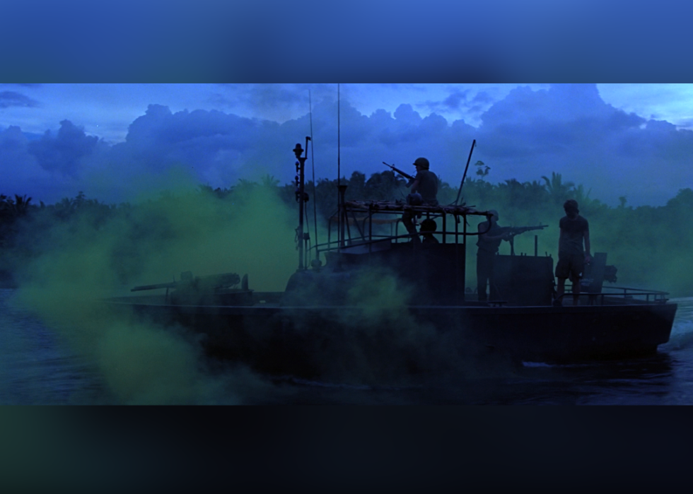 A silhouette of a boat with soldiers floats along a river in front of a deep blue and greeen sky