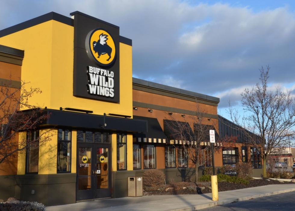 A brown and yellow building with black awnings over windows. A large Buffalo Wild Wings logo is mounted above the entrance. The logo features the text Buffalo Wild Wings in white lettering.