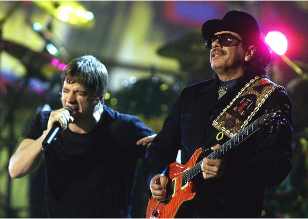 Santana plays guitar and Rob Thomas sings onstage.