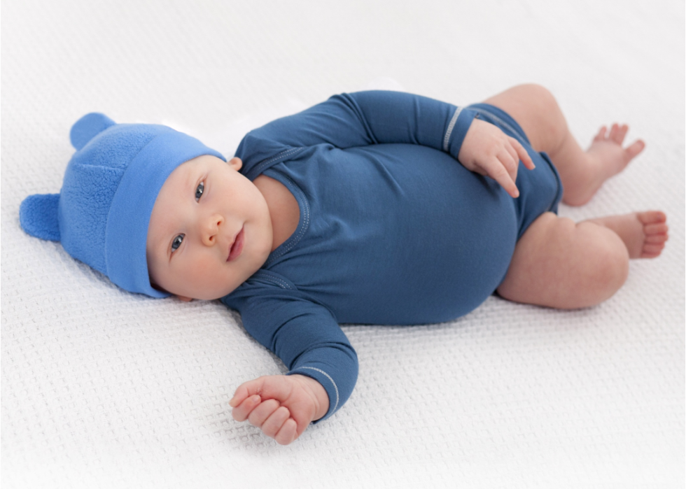 A baby boy wearing all blue outfit lying down on his back. 