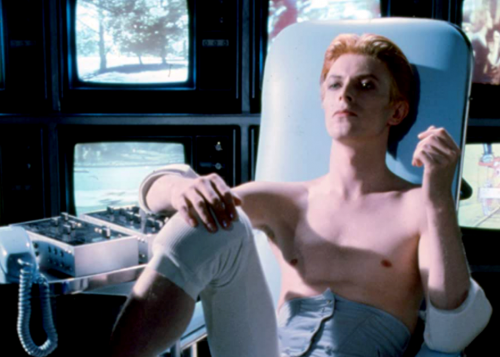 A shirtless Bowie sits back on a chair in a still from the film The Man Who Fell to Earth.