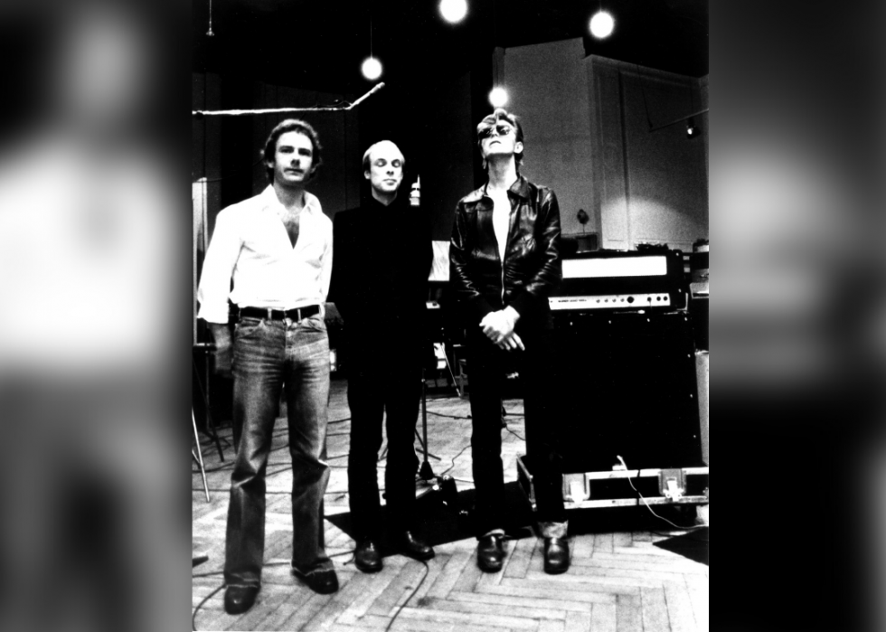 Two men and Bowie stand in a recording studio. 