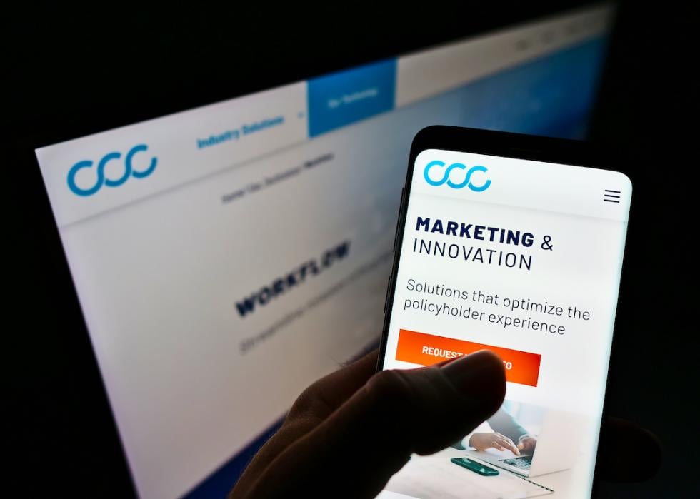 Person holding cellphone with website and logo of software company CCC Intelligent Solutions Holdings on screen.