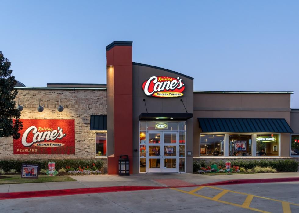 One story, large, brick building with a large door and windows on the right side. The neon sign above the door says Raising Cane's Chicken Fingers. 