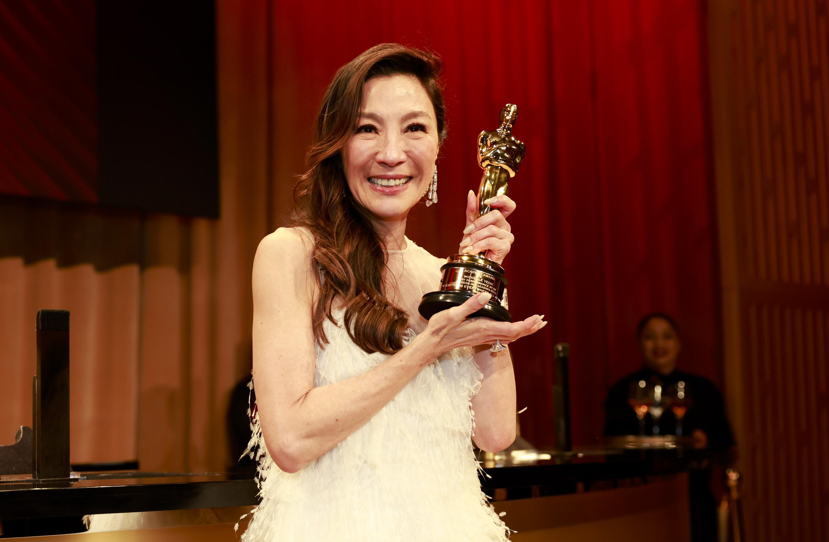 Michelle Yeoh in a white strapless feather gown posing with an Academy Award.