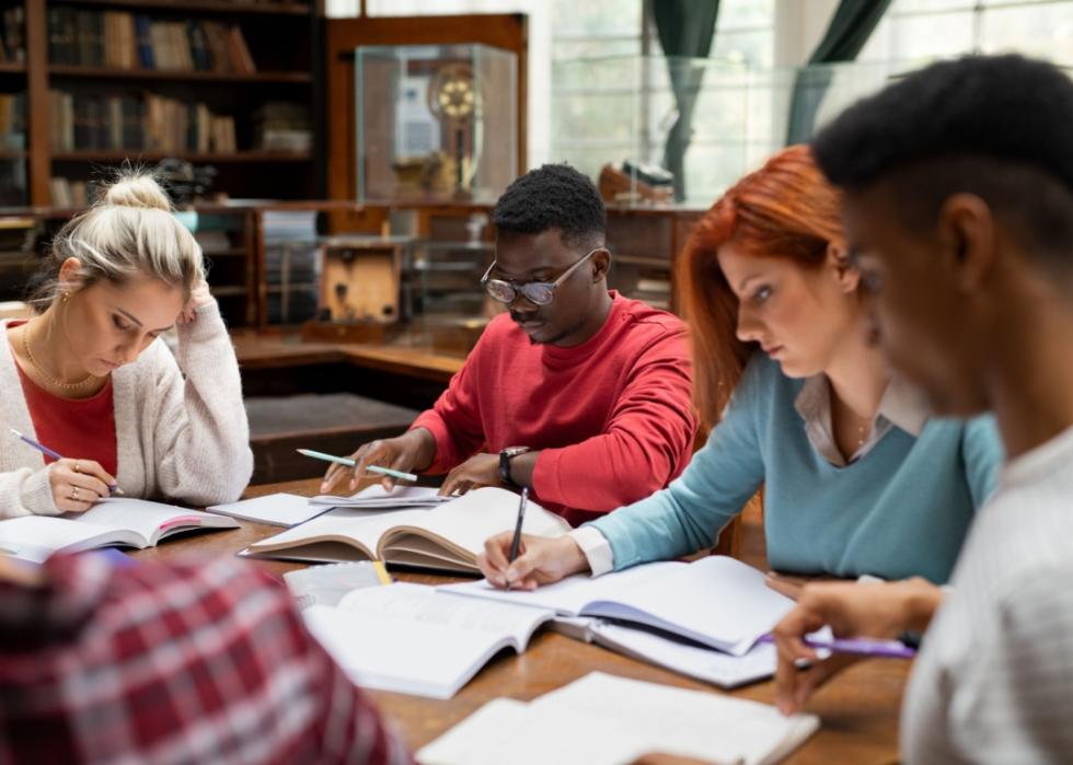 Four students sitting together at the table. Some are reading when others are writing in their notebooks.