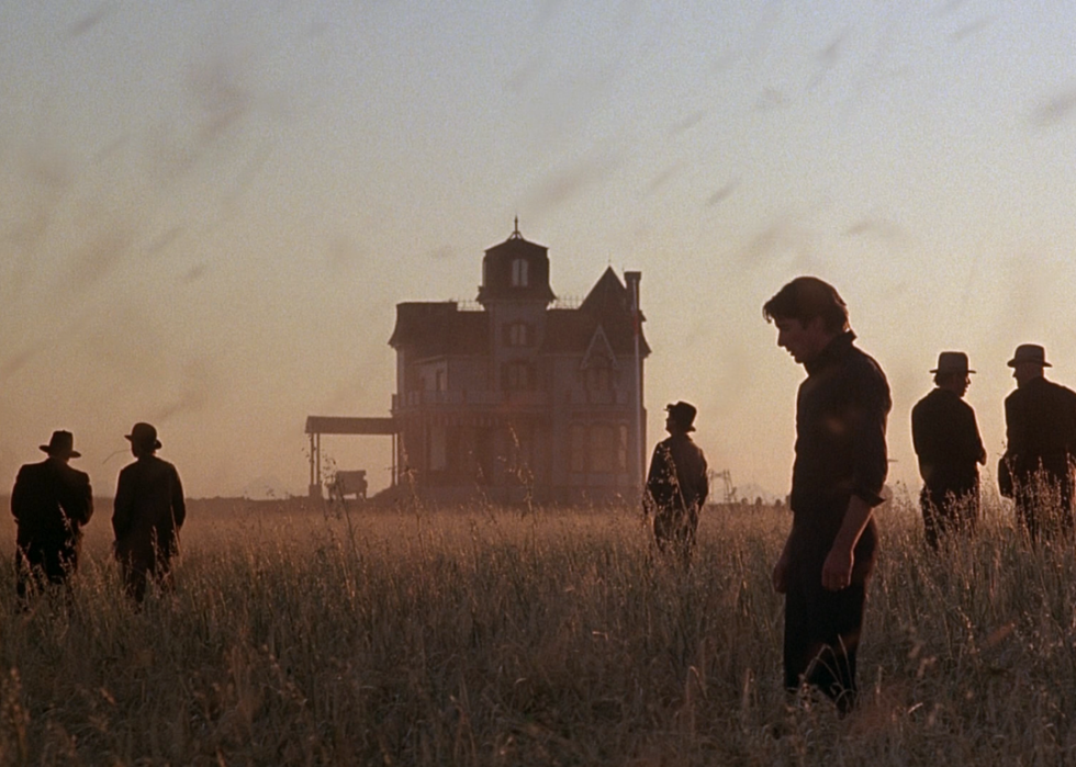 A silhouette of Richard Gere standing in a wheat field with an old farmhouse in the distance