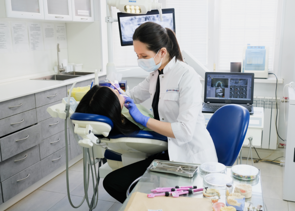A dentist works on the teeth of a patient in her chair.