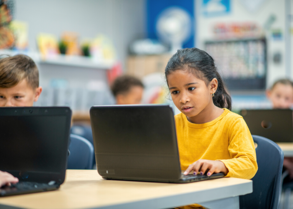 Elementary school students concentrate on laptops in a classroom.