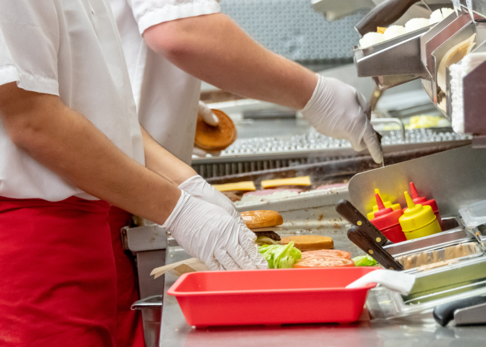 A close-up of fast-food workers' hands in gloves assembling a meal.