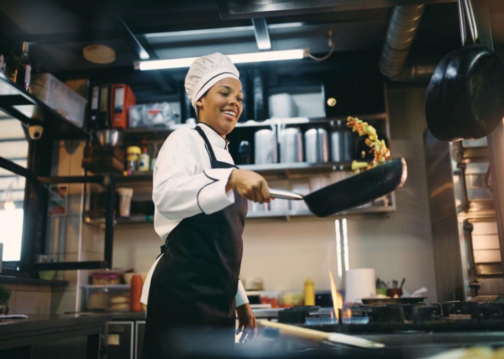 Black woman chef holding a pan with vegetables in the kitchen at restaurant.