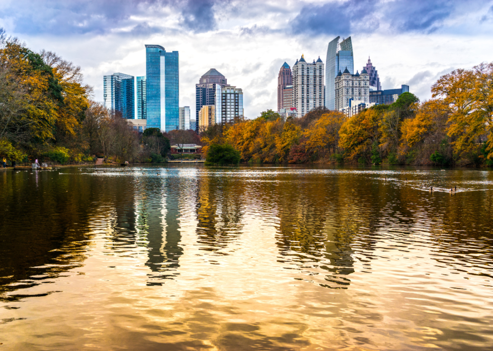 Skyscrapers by the body of water surrounded by trees in fall. 