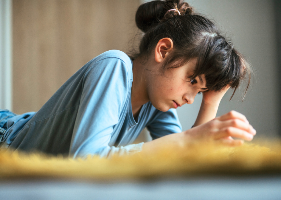 A young girl lying on her stomach. She is resting her head on one hand while looking down at something in front of her. 