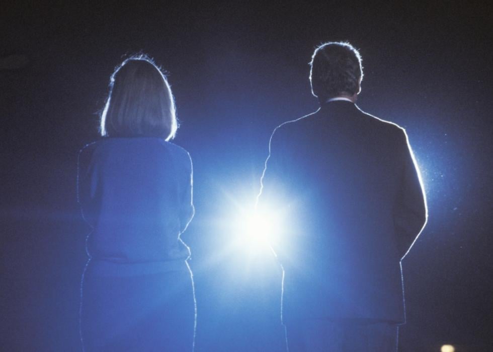 From behind, two silhouettes stand in front of a bright light. 