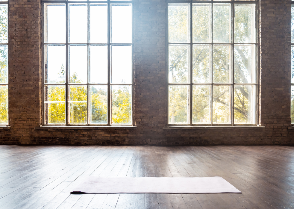 A yoga mat on a wooden floor in front of big windows.
