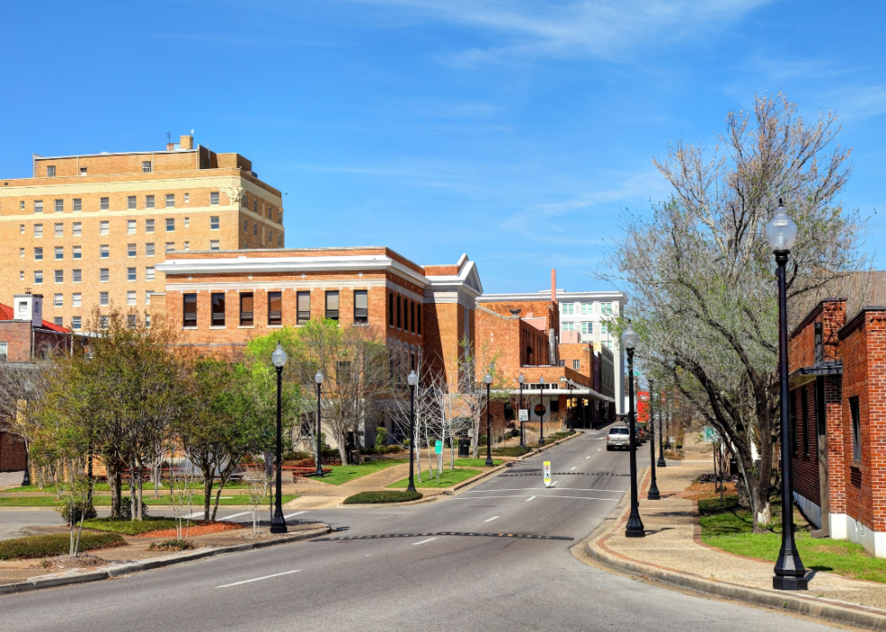 The street lined with tall buildings, few trees and streetlights.