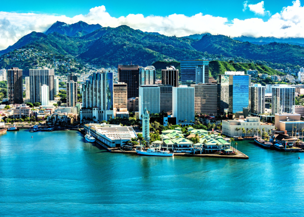 Tall buildings by the water with green mountains in the background.