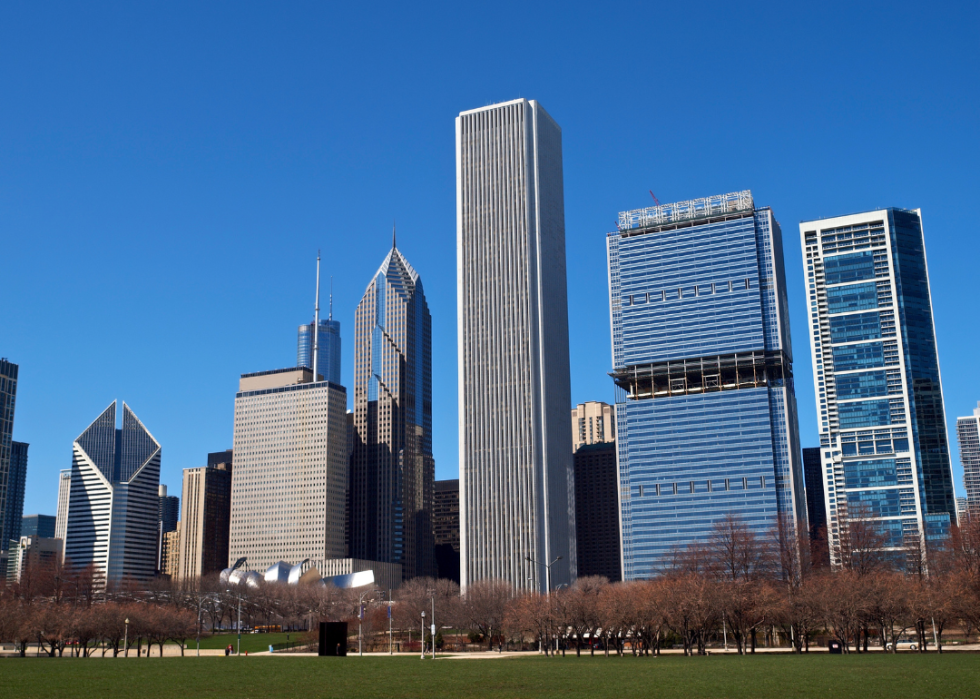 Modern steel and glass city skyscrapers by large field of grass in the foreground. 