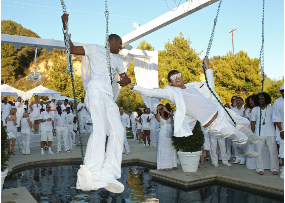 Guests dressed all in white frolic on swings by a pool.