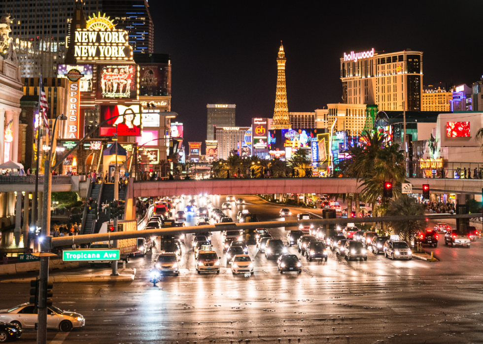 A wide road with several lanes with heavy traffic at night with buildings in the background.