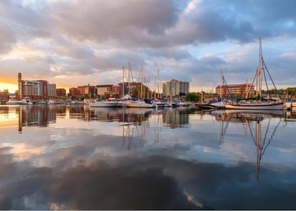 Sunset over a harbor filled with sailboats. The city skyline is visible in the distance. 