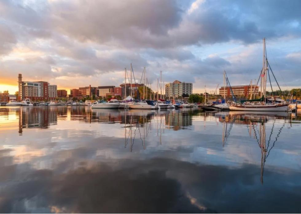 Sunset over a harbor filled with sailboats. The city skyline is visible in the distance.