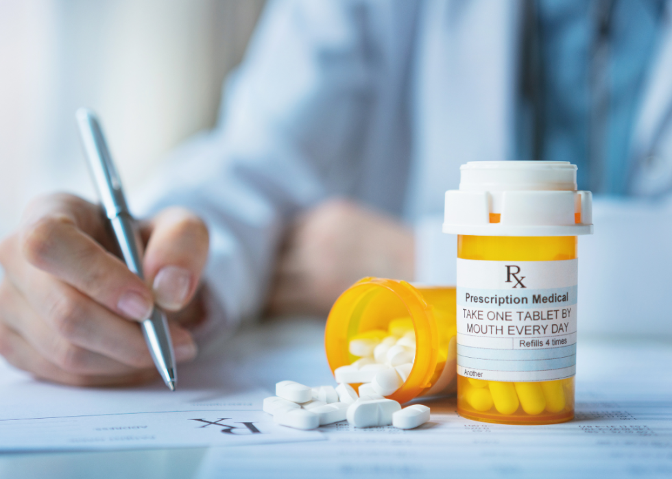 A closeup of hands writing holding a pen and two orange bottles of medication on the table.  