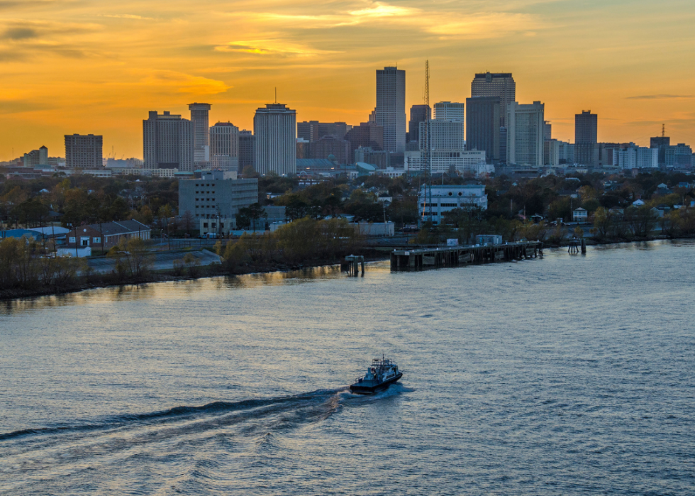 City skyline with sunset in background and boat on a river in the foreground.