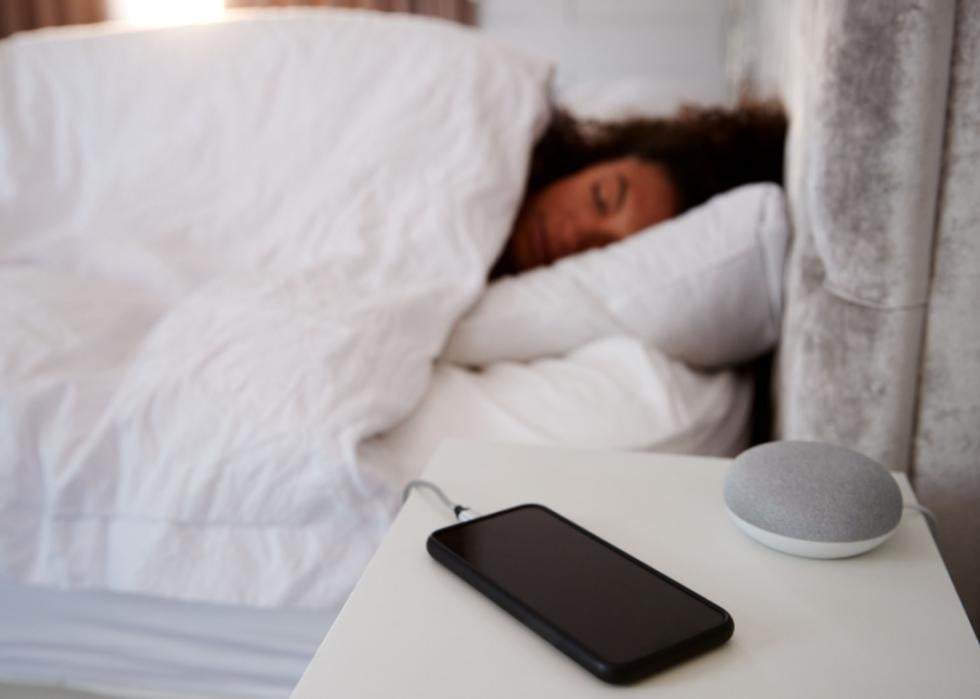 A smartphone charging on a woman's nightstand while she sleeps.
