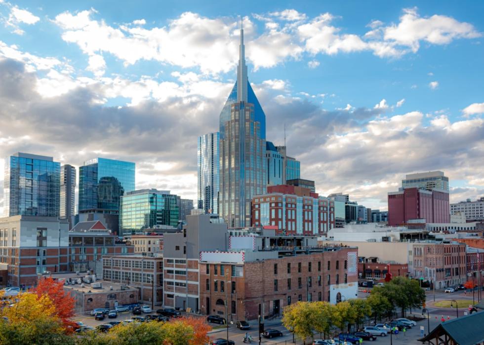 A cityscape with tall skyscraper. The surrounding area has a mix of modern and older, brick buildings and trees with fall foliage.