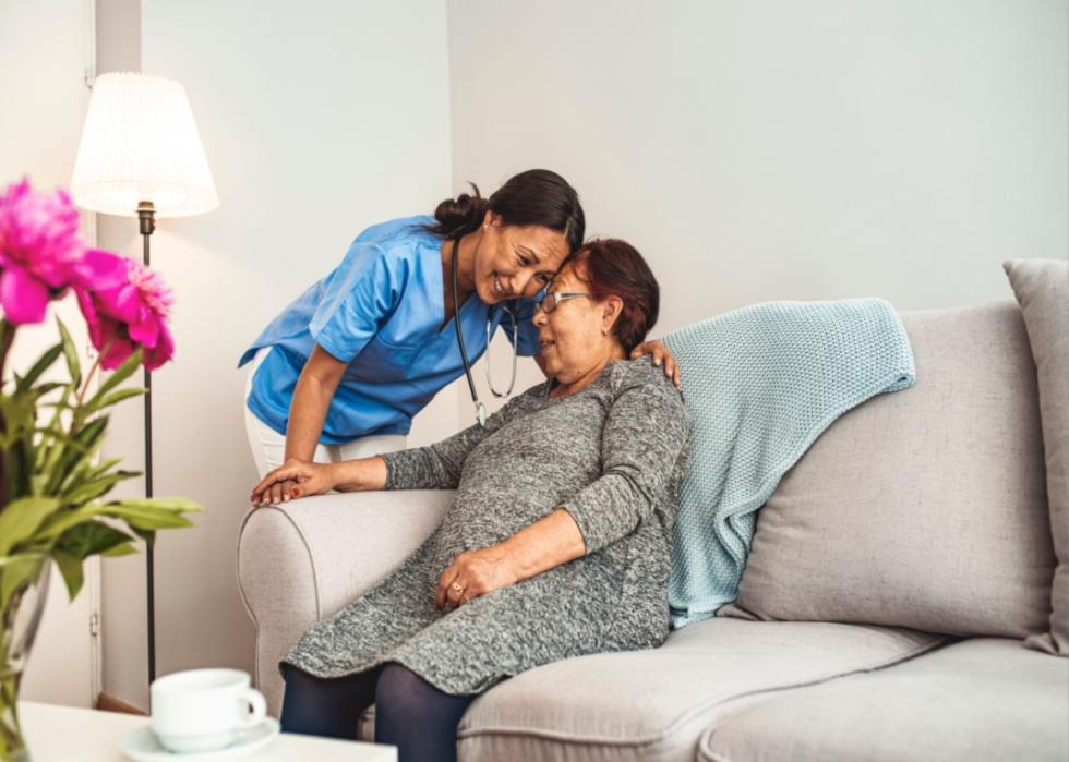 A nurse hugging a woman on a couch.