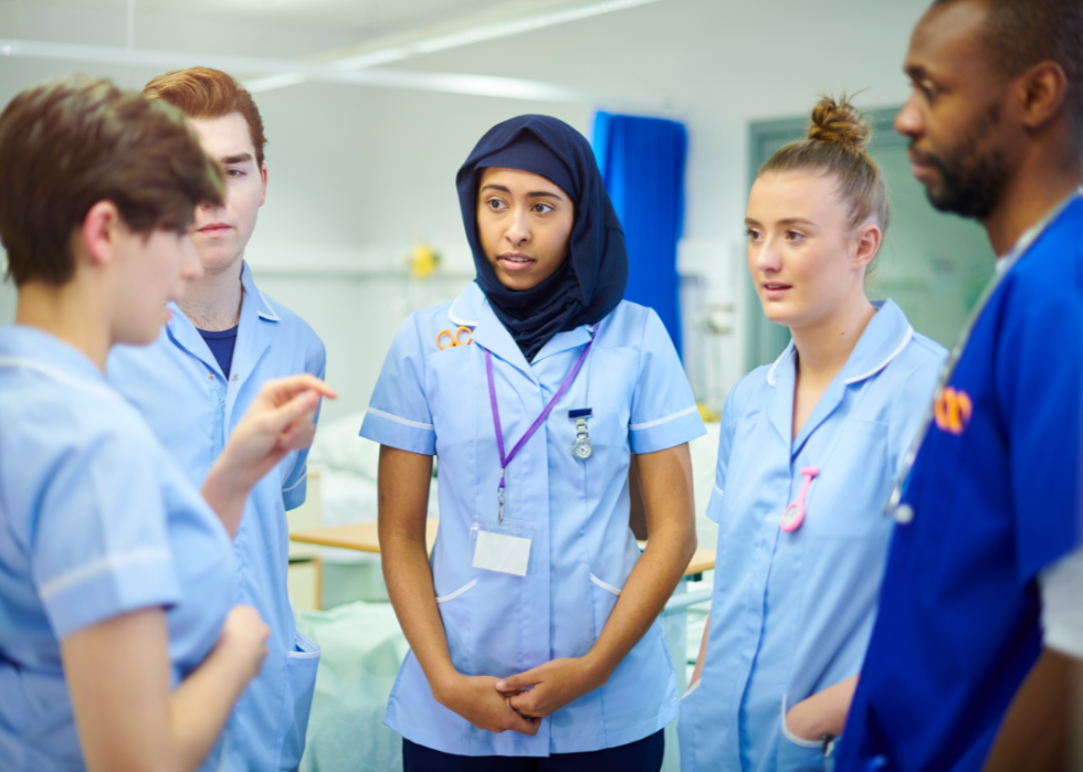 Two female young nurses and two young male nurses in a circle listening to the nurse talking to them.