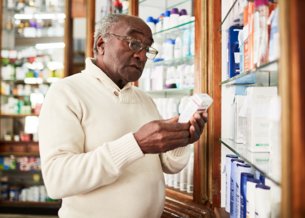 An older African American man holding a bottle of medication in a pharmacy. 