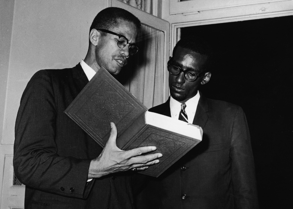 Malcolm X holds an open copy of the Koran as he speaks to an unidentified man at African Summit Conference in Cairo, Egypt, July 1964.