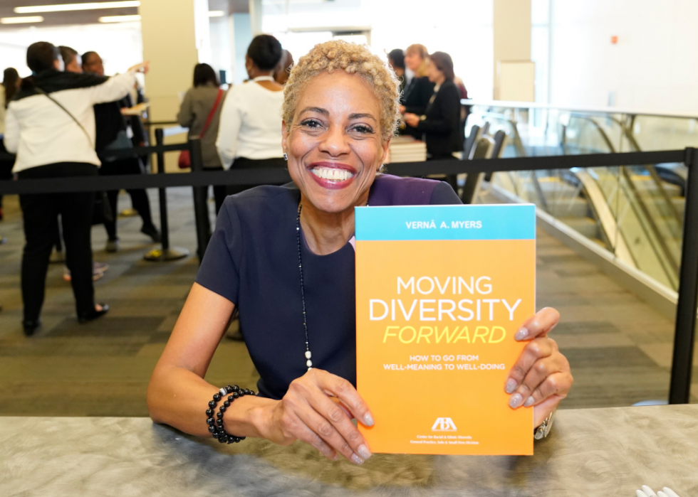 Verna Myers, smiling, holds her book, Moving Diversity Forward: How to Go From Well-Meaning to Well-Doing during a 2020 conference.
