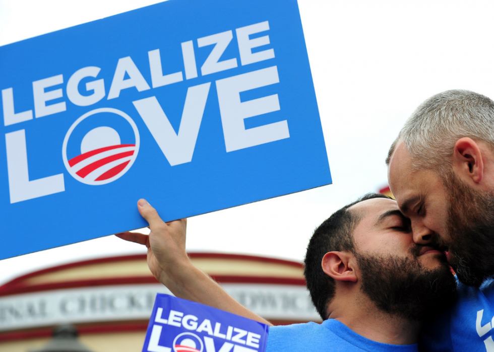 Two men kiss in front of a Chick-fil-A, holding a sign that says Legalize Love.