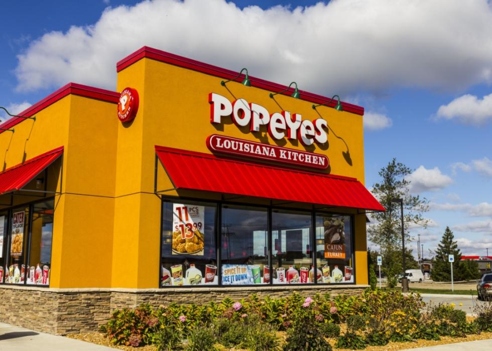 A large golden yellow building with red trim and red awnings over the windows. There is a large white Popeyes logo and Louisiana Kitchen written underneath it.