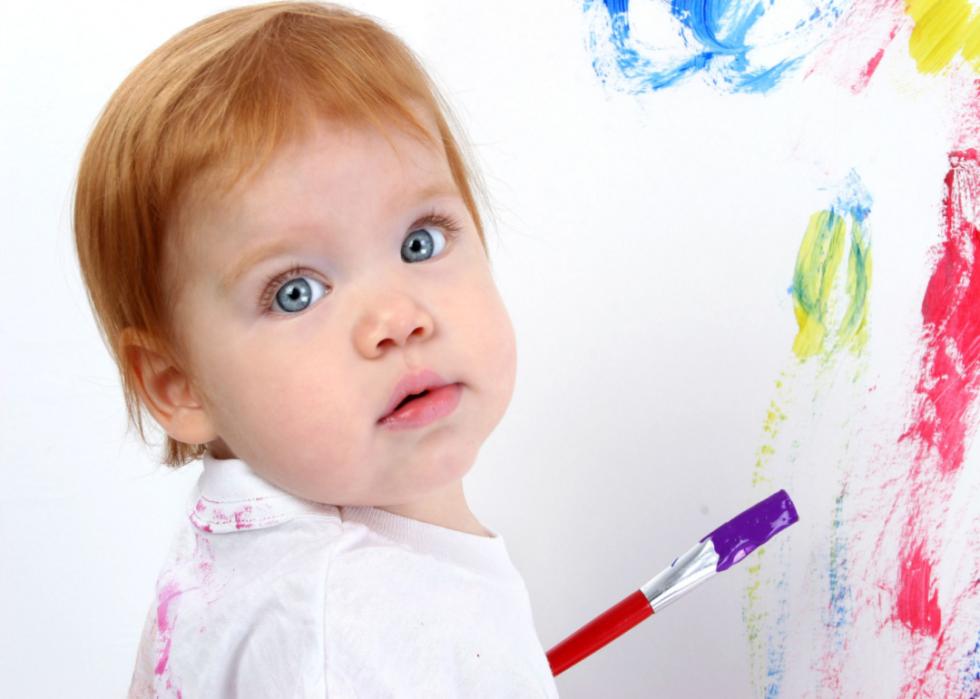 Redhead baby painting at poster board.
