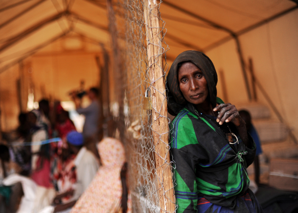 A Somali woman in a large tent with many people in the background at a refugee camp.