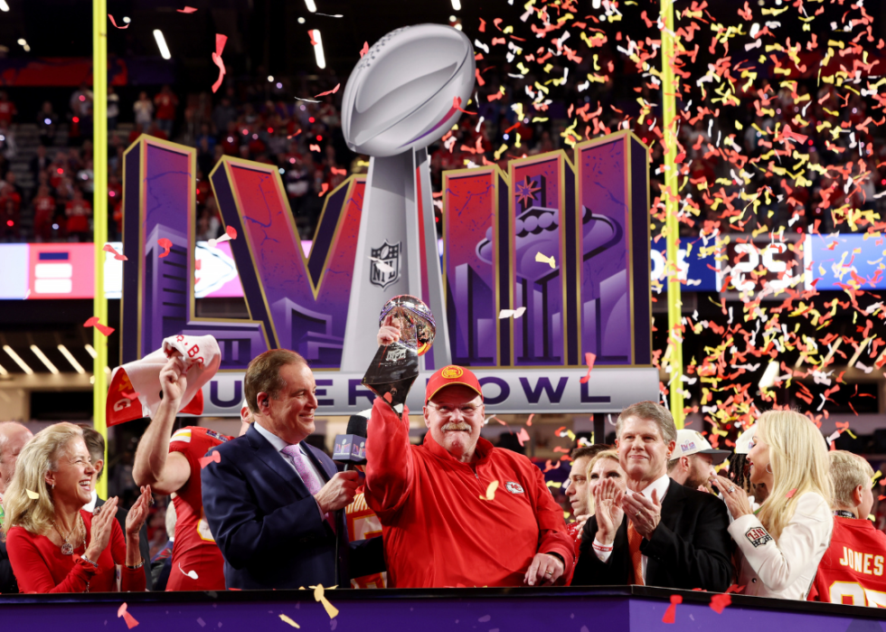 Andy Reid holding a superbowl trophy on the field.