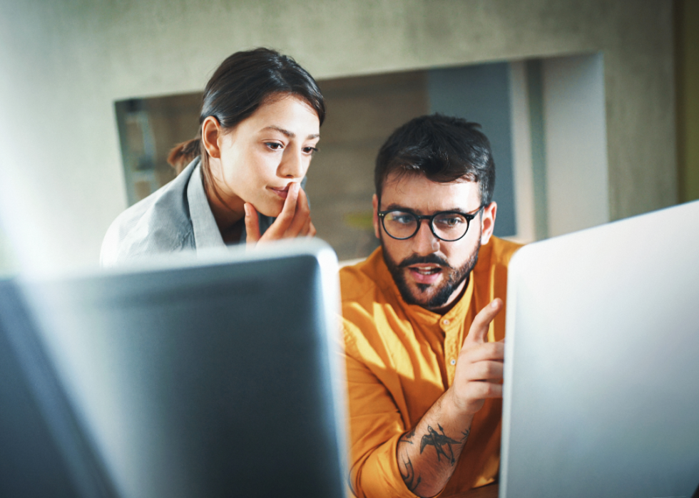 Two young professionals discuss what they are seeing on their computer screens.