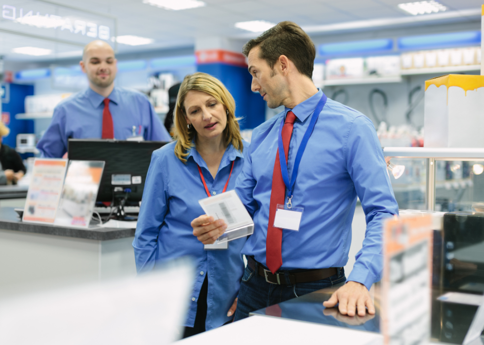 A woman and a man wearing blue shirts and badges are both looking at the acrylic stand in a store. 