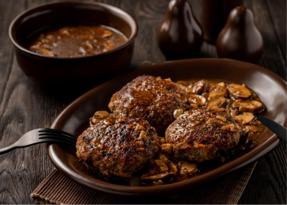 An oval brown plate with flattened patties of brown meat and mushroom sauce. 