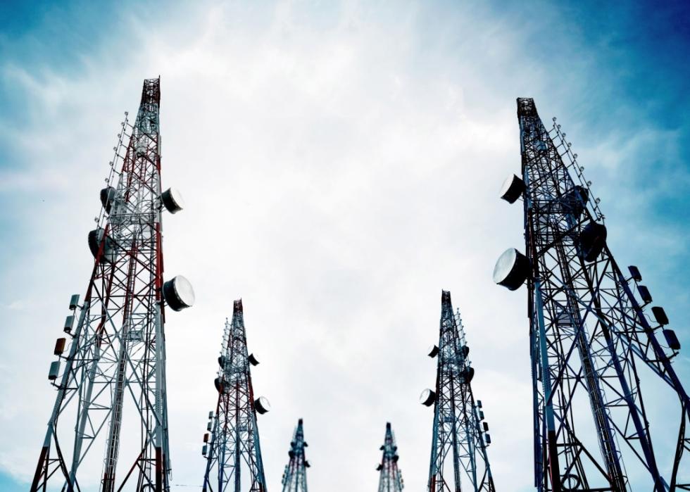 Tall telecommunication towers with TV antennas and satellite dish on clear blue sky.