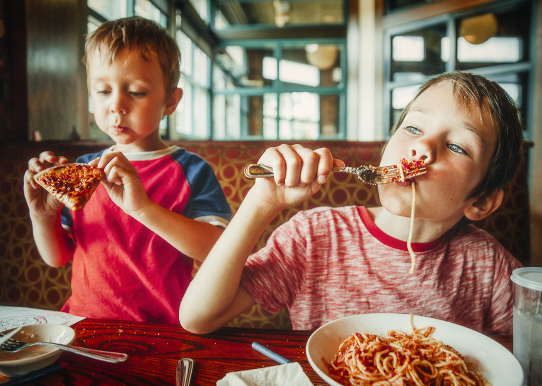 Two young boys eating pizza and pasta.