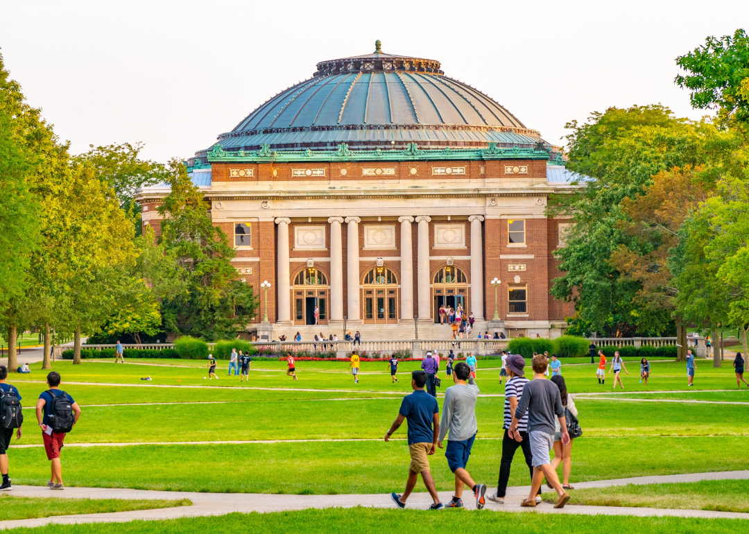 Students walking outdoors on a quad at the University of Illinois Urbana-Champaign college campus.