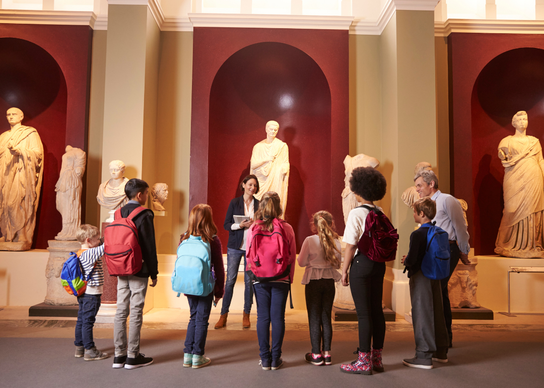 A museum guide explaining an exhibit to a group of students and their teacher.